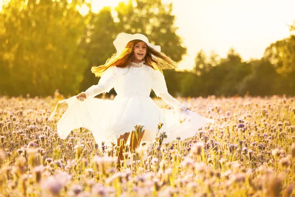 Happy little  girl in a white dress running on field at sunset — Stock Photo, Image