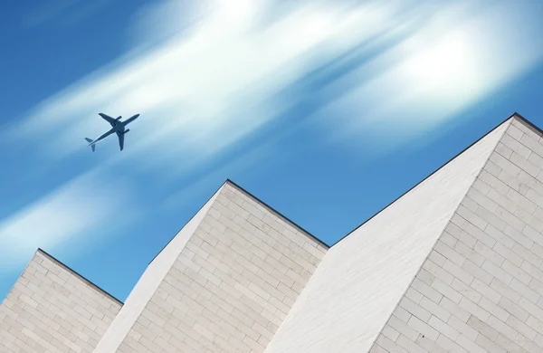 Airplane flying over modern building — Stock Photo, Image