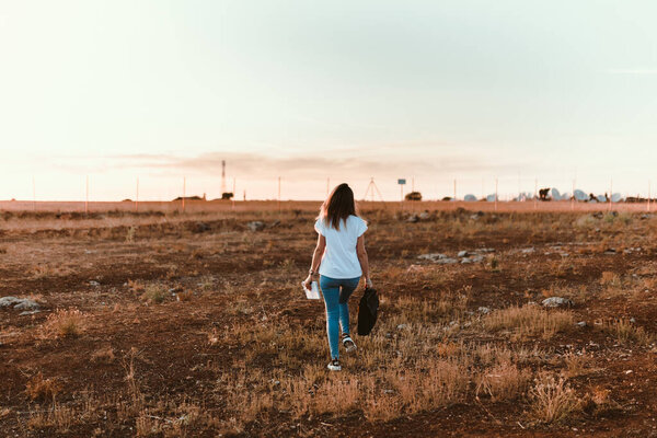 Young woman walking through the field with her laptop case