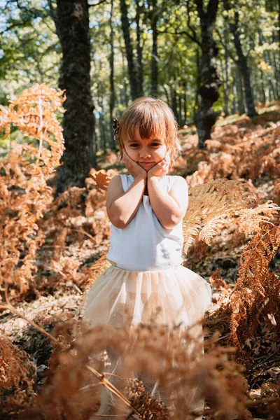 Malá kavkazská holčička dřepící v lese mezi kapradinami — Stock fotografie
