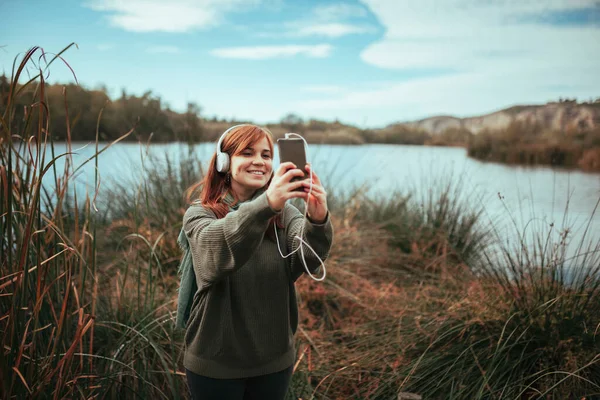Genç bir kadın gölün kenarında akıllı telefonuyla selfie çekiyor. — Stok fotoğraf