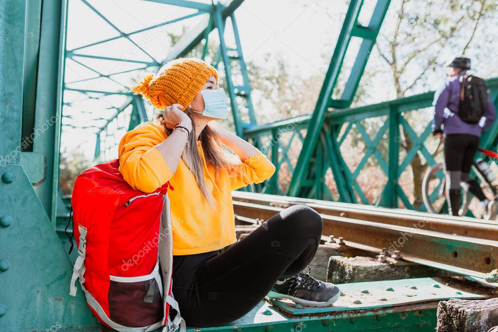 Woman trekking rests on an abandoned railway track with her surgical mask