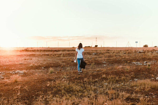 Young woman walking through the field with her laptop case