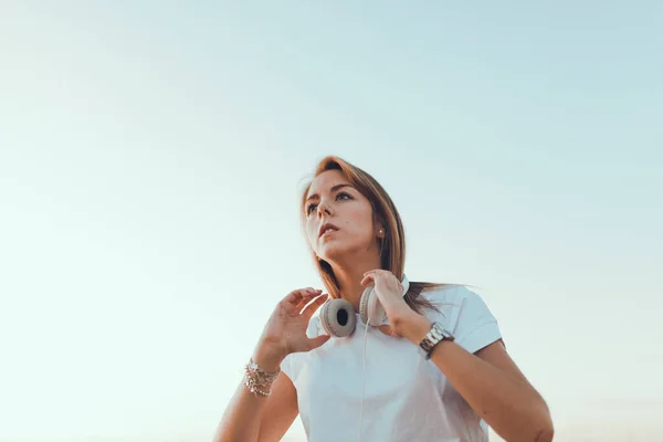 拿着手提电脑的年轻女人用耳机听外面的交流 — 图库照片