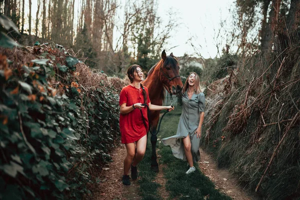 田舎で二人の女友達が馬とおしゃべりしたり乗ったり — ストック写真