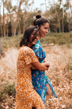 Ormanda birbirini okşayan iki genç lezbiyen uzun elbiseler giyiyor.