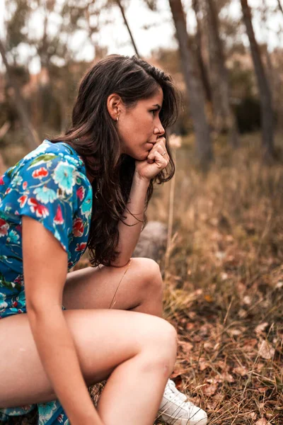 Ritratto all'aperto di una bella donna bruna che indossa un vestito seduta in un tronco nel bosco — Foto Stock