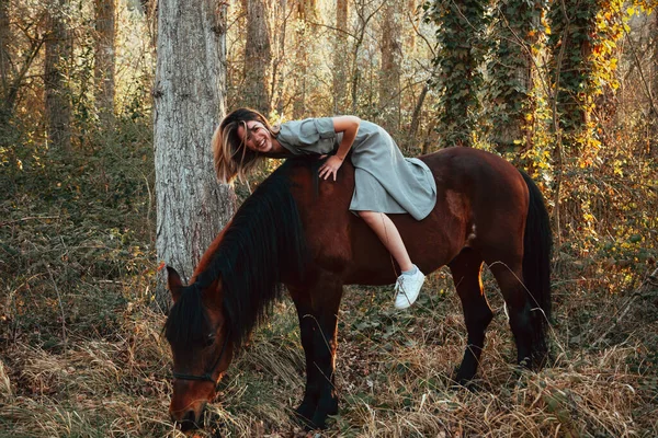 Belle jeune femme étreignant cheval brun et portant une robe — Photo