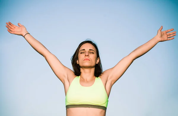 Mujer morena en ropa deportiva haciendo ejercicio de estiramiento con los brazos hacia arriba mientras hace ejercicio — Foto de Stock