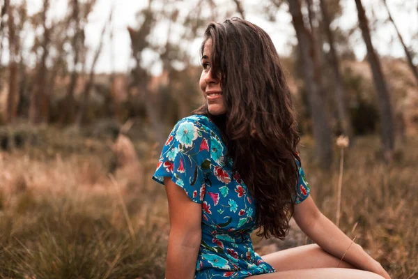 Außenporträt einer schönen brünetten Frau in einem Kleid, die in einem Baumstamm im Wald sitzt — Stockfoto