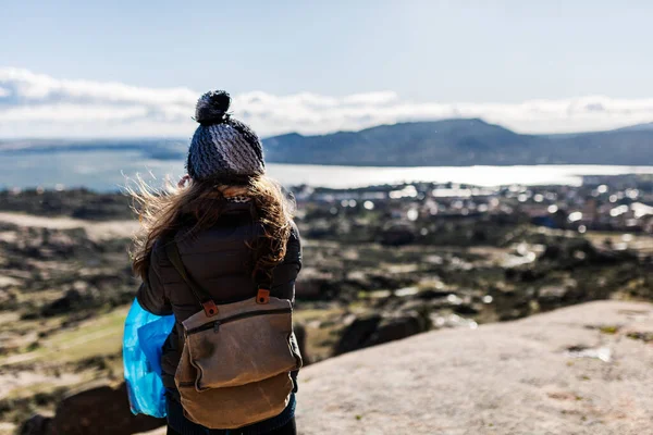 Yürüyüş ekipmanlarıyla genç aktif bir kadın oturmuş, dinleniyor ve göllere ve dağlara bakıyor.