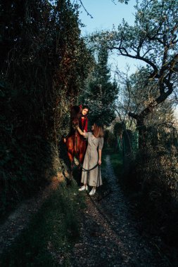 İki kadın arkadaş sohbet ediyor ve atlarıyla kırsalda geziyorlar.