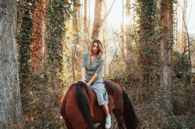 Güzel genç bir kadın kahverengi atına biniyor ve elbise giyiyor.