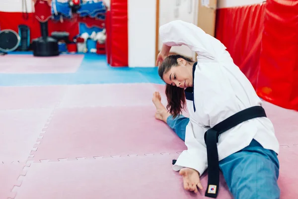 Young woman stretching in a dojo wearing taekwondo dobok — Stock Photo, Image
