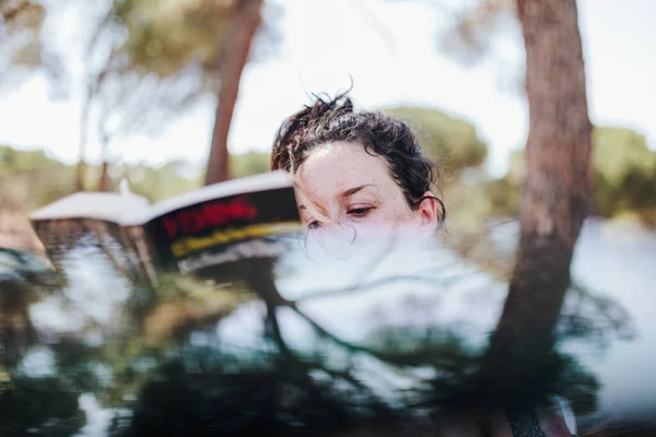 Jovem mulher lendo um livro em um parque em um dia ensolarado — Fotografia de Stock