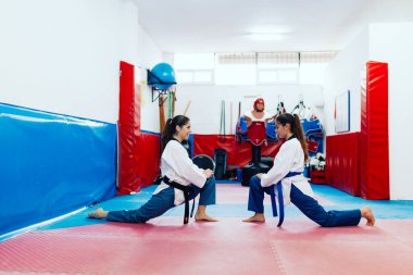 Genç kadınlar bir dojo 'da tekvando kıyafetleri giyerek geriniyorlar.