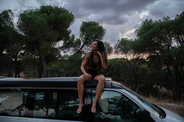 Mujer sentada en el techo de una caravana en el bosque al atardecer —  Fotos de Stock