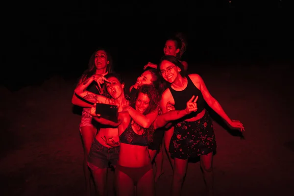 Grupo de jovens mulheres se divertindo em uma festa à beira do lago à noite com uma luz vermelha — Fotografia de Stock