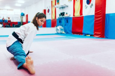 Genç bir kadın dojo 'da gerinirken tekvando salonunu giyiyor.