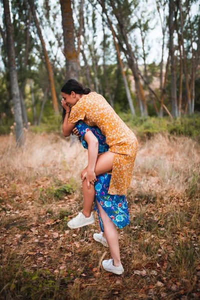 Mulher piggybacking feliz namorada enquanto desfruta na floresta — Fotografia de Stock