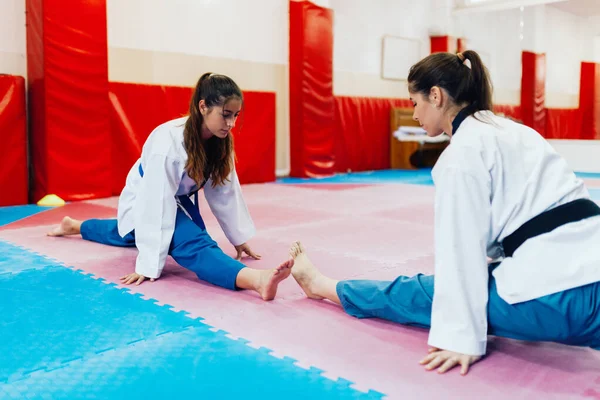 Νεαρές γυναίκες Στραντλ τέντωμα σε ένα dojo φορώντας taekwondo dobok — Φωτογραφία Αρχείου