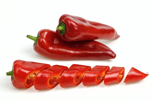 Pointy red peppers and one cut into pieces, on white background. — Stock Photo, Image