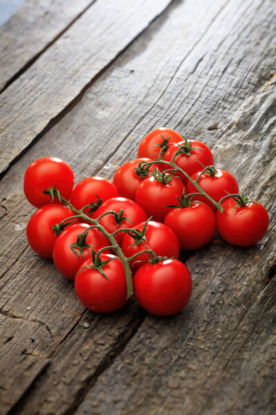 Две связки красных помидоров черри на деревянной поверхности

