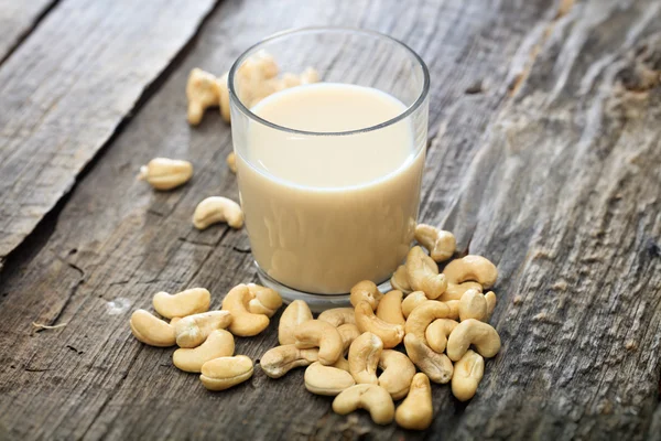 Heap van rauwe cashewnoten en een glas cashewnelk, op houten ondergrond — Stockfoto