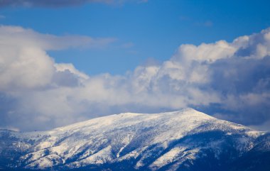 Karlı dağ silsilesi ile mavi gökyüzü ve bulutlar.