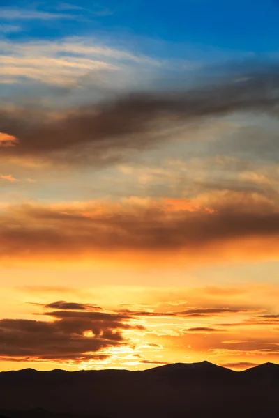 Sun behind dark mountain silhouettes, with colorful sky and clouds — Stock Photo, Image