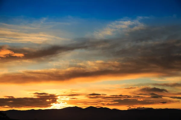 Soleil derrière des silhouettes sombres de montagne, avec ciel coloré et nuages — Photo