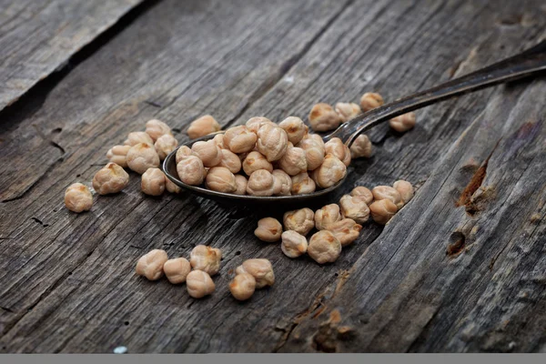 Garbanzo beans on spoon, on wooden surface. — Stock Photo, Image