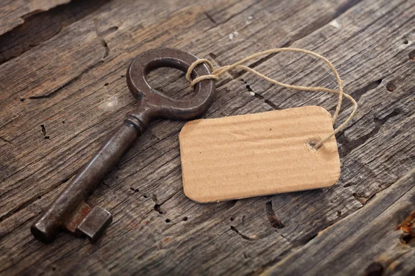 Roestige oude sleutel met een tag op houten oppervlak — Stockfoto