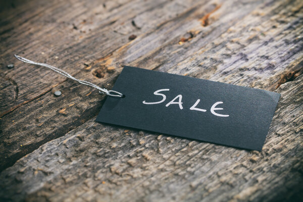 Closeup of pricing tag with twine and "Sale" text on wooden background