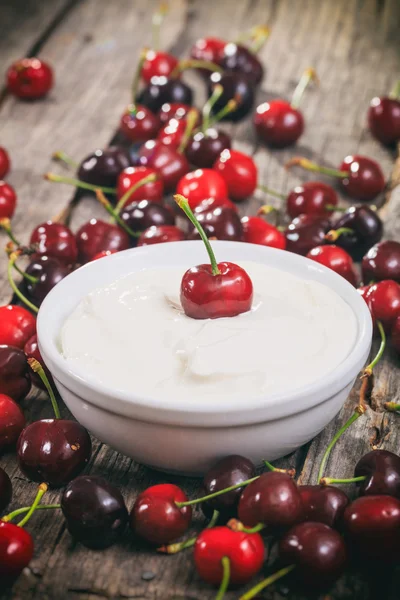 Creamy yogurt with cherries, on wooden surface.