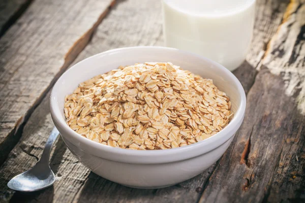 Bowl of oat flakes and glass of milk, on wooden surface. — Stock Photo, Image