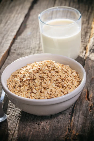 Bowl of oat flakes and glass of milk, on wooden surface. — Stock Photo, Image