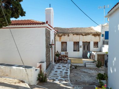 Yunanistan 'ın Messaria kenti Kythnos' taki Yunan Ortodoks Hıristiyan Şapeli 'nin yanındaki eski paslı geleneksel çatılı ev. Asfalt boş avlu boyalı resimler, sandalyeler, bitkiler.
