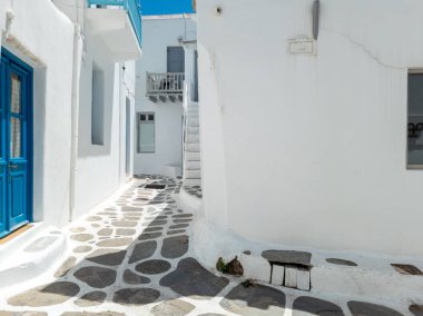 Yazın güneşli bir yaz günü merdivenleri olan boş dar bir sokak beyazlatılmış evleri olan tipik bir şehir. Geleneksel Yunan binaları, kozmopolit tatil beldesi Mykonos adası Cyclades Yunanistan 'da inşa ediliyor.
