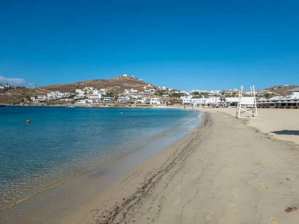 Ornos boş tropikal kumlu sahil cankurtaran kulesi şeffaf sakin deniz açık mavi gökyüzü beyazlatılmış binalar Mykonos adası, Cyclades Yunanistan için reklam. Yaz tatili için tatil yeri.