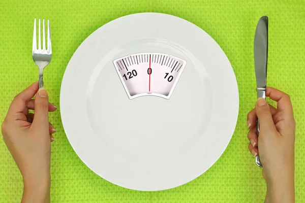 Manos y plato con báscula de pesaje sobre la mesa —  Fotos de Stock