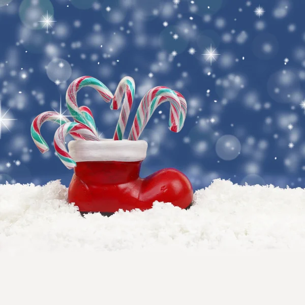 Bastones de caramelo de Navidad en bota de santas en la nieve — Foto de Stock
