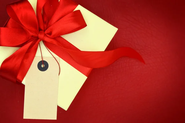 Gift box with blank tag on red background — Stock Photo, Image