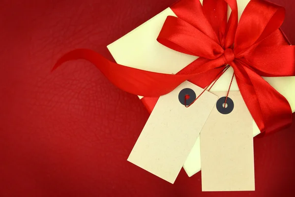 Gift box with two blank tags and ribbon on red background — Stock Photo, Image