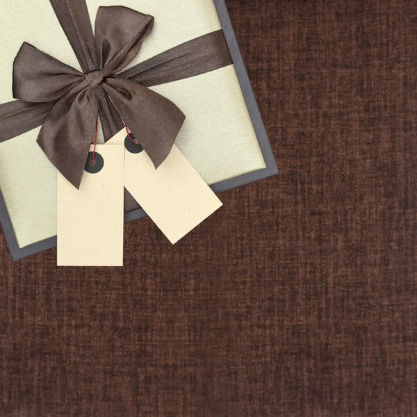 Подарочная коробка с лентой и двумя пустыми бирками на коричневом — стоковое фото