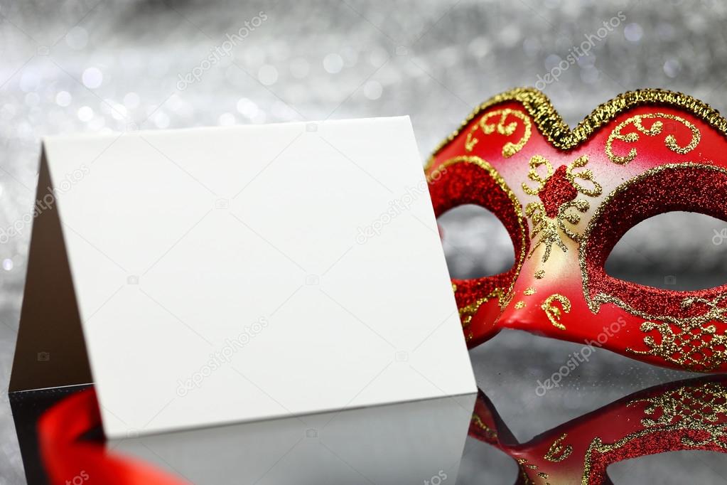 Vintage carnival mask and white blank card in front of glittering background