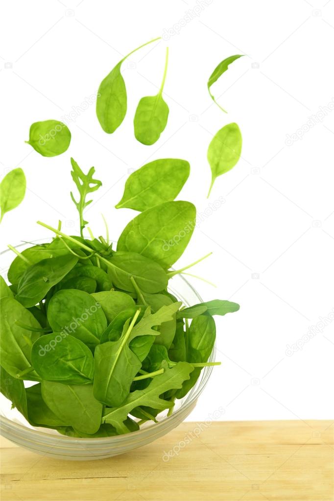 Fresh green salad with some leaves flying out of a bowl isolated