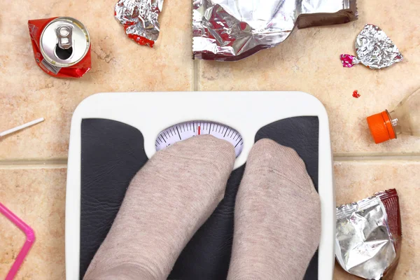 Pieds sur la balance de salle de bain avec ordures malbouffe autour — Photo