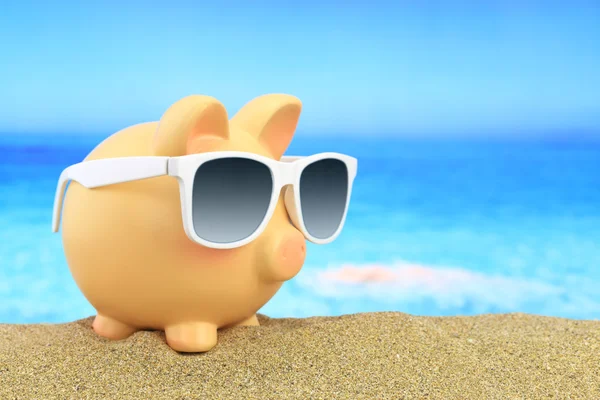 Summer piggy bank with sunglasses on beach — Stock Photo, Image