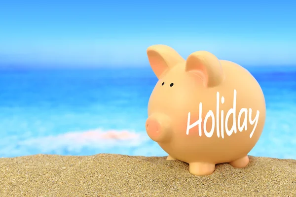 Word vakantie geschreven op piggy bank op het strand — Stockfoto